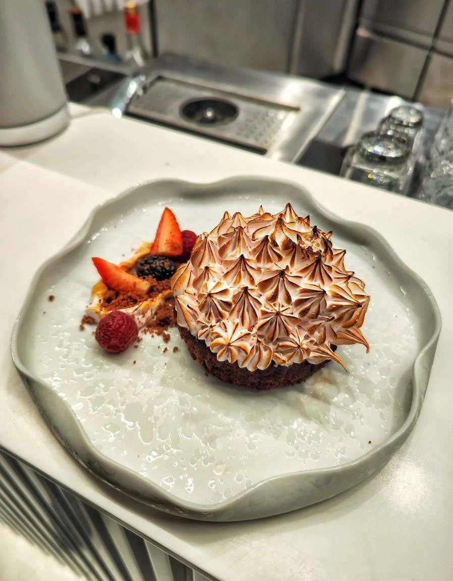 Baked Alaska with toasted meringue peaks on a chocolate base, with strawberries and berries