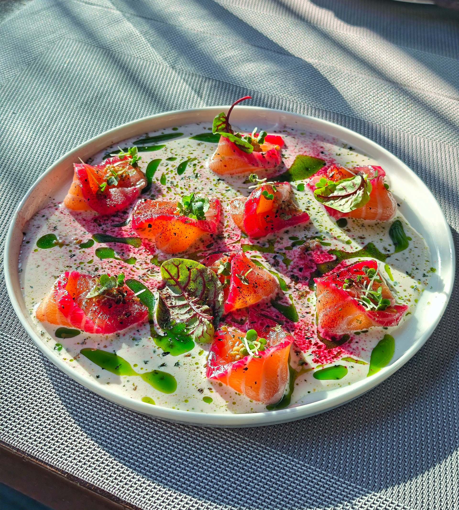 Σολομός μαριναρισμένος με παντζάρι, σε φέτες, με μυρωδικά και πράσινο λάδι σε λευκό πιάτο