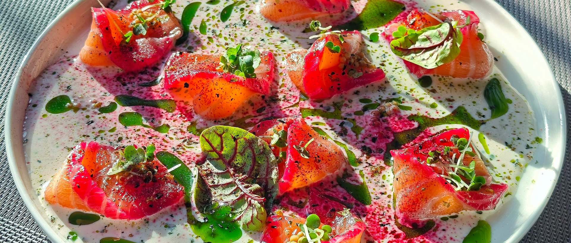 Beetroot cured salmon, sliced, with herbs and green oil on a white plate