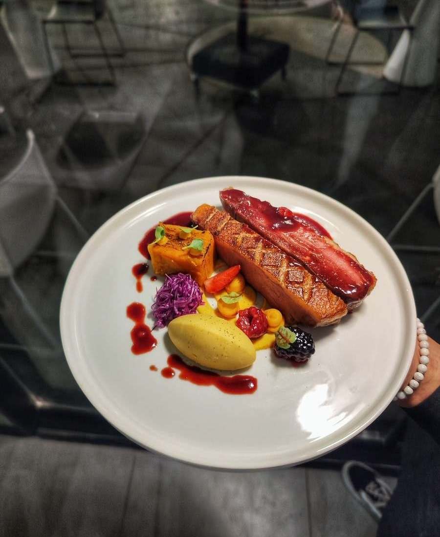 Sliced duck fillet with sweet potato purée, red cabbage and a dark berry sauce on a white plate