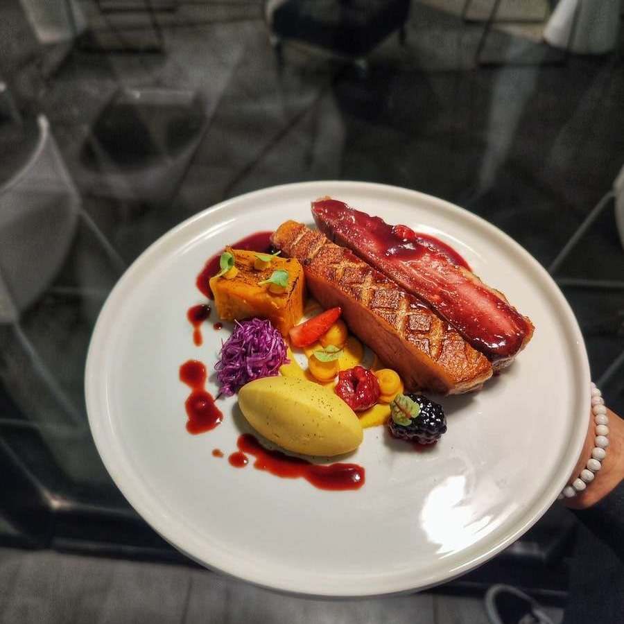 Нарезанное утиное филе с пюре из батата, краснокочанной капустой и тёмным ягодным соусом на белой тарелке
