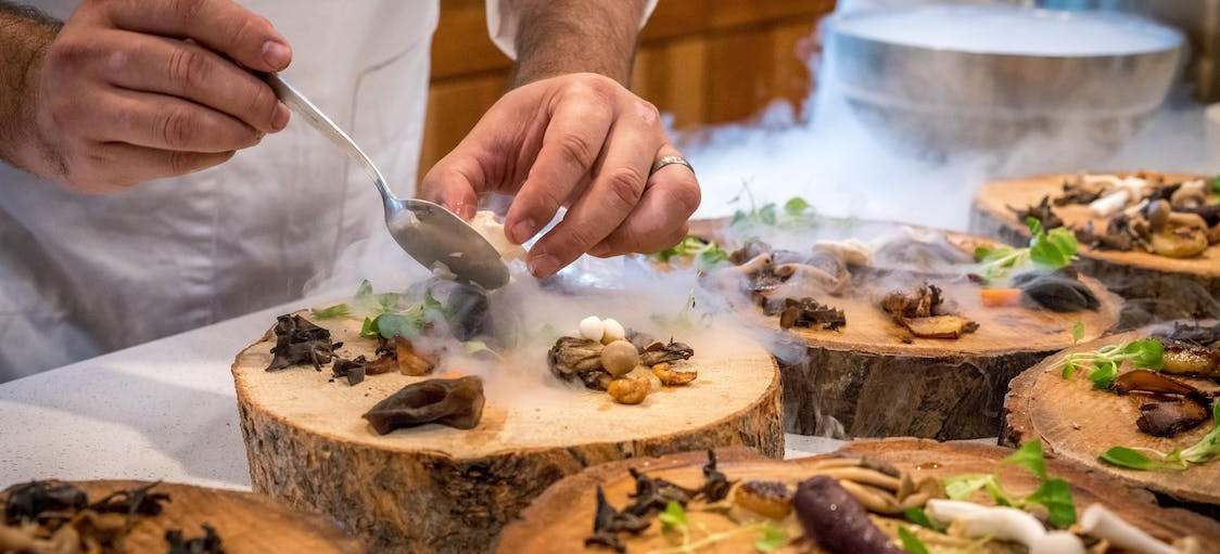Σεφ ολοκληρώνει με ένα κουτάλι πιάτα με μανιτάρια πάνω σε ξύλινες σανίδες