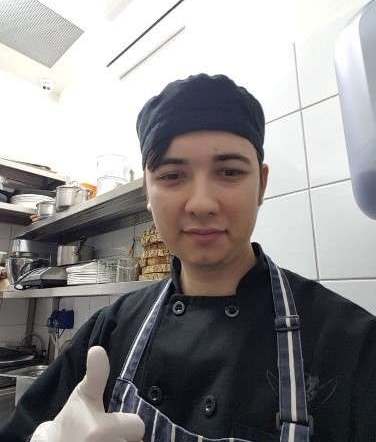 Eugene Charalampous in a black chef jacket giving a thumbs up in a kitchen