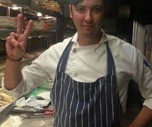 Eugene Charalampous in a chef jacket and striped apron in a restaurant kitchen