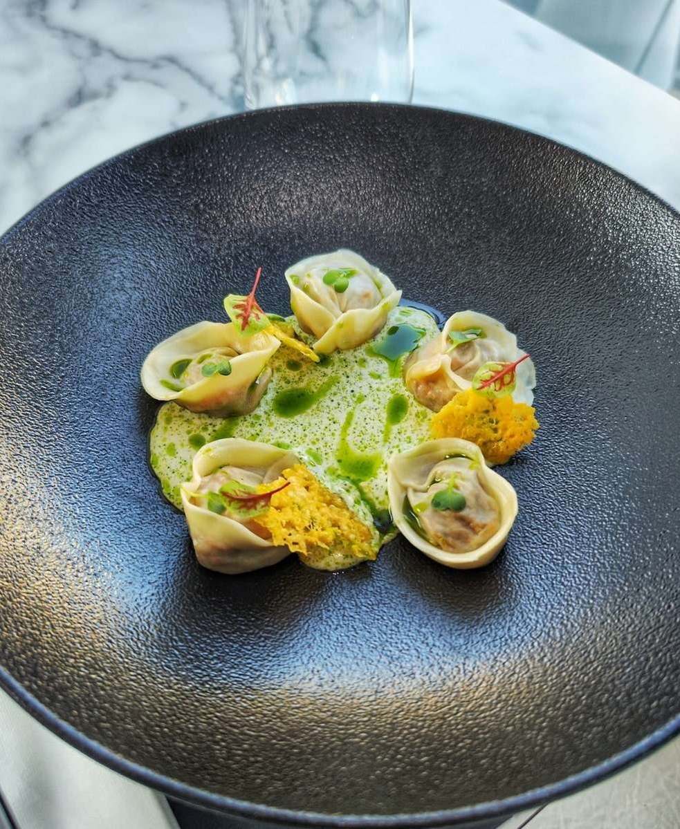 Folded pork belly dumplings in clam chowder with parsley oil on a black plate