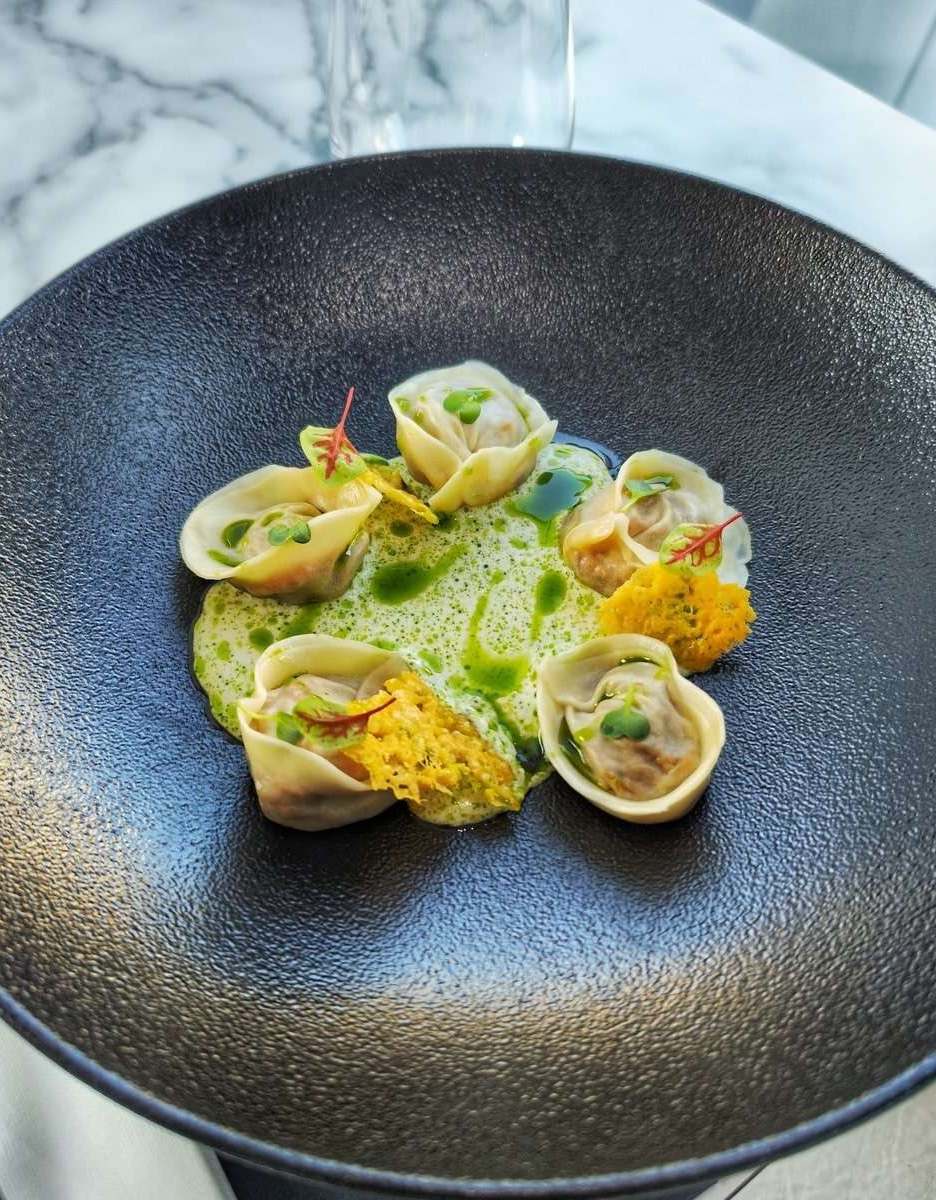Folded pork belly dumplings in clam chowder with parsley oil on a black plate