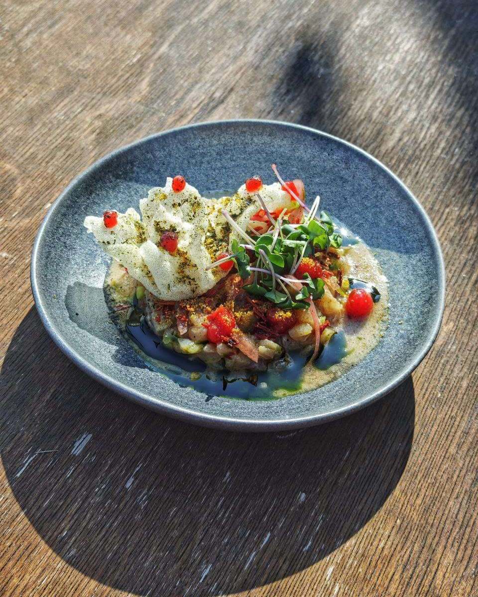 Seabass ceviche, a shared plate finished with herbs, on a wooden table in daylight