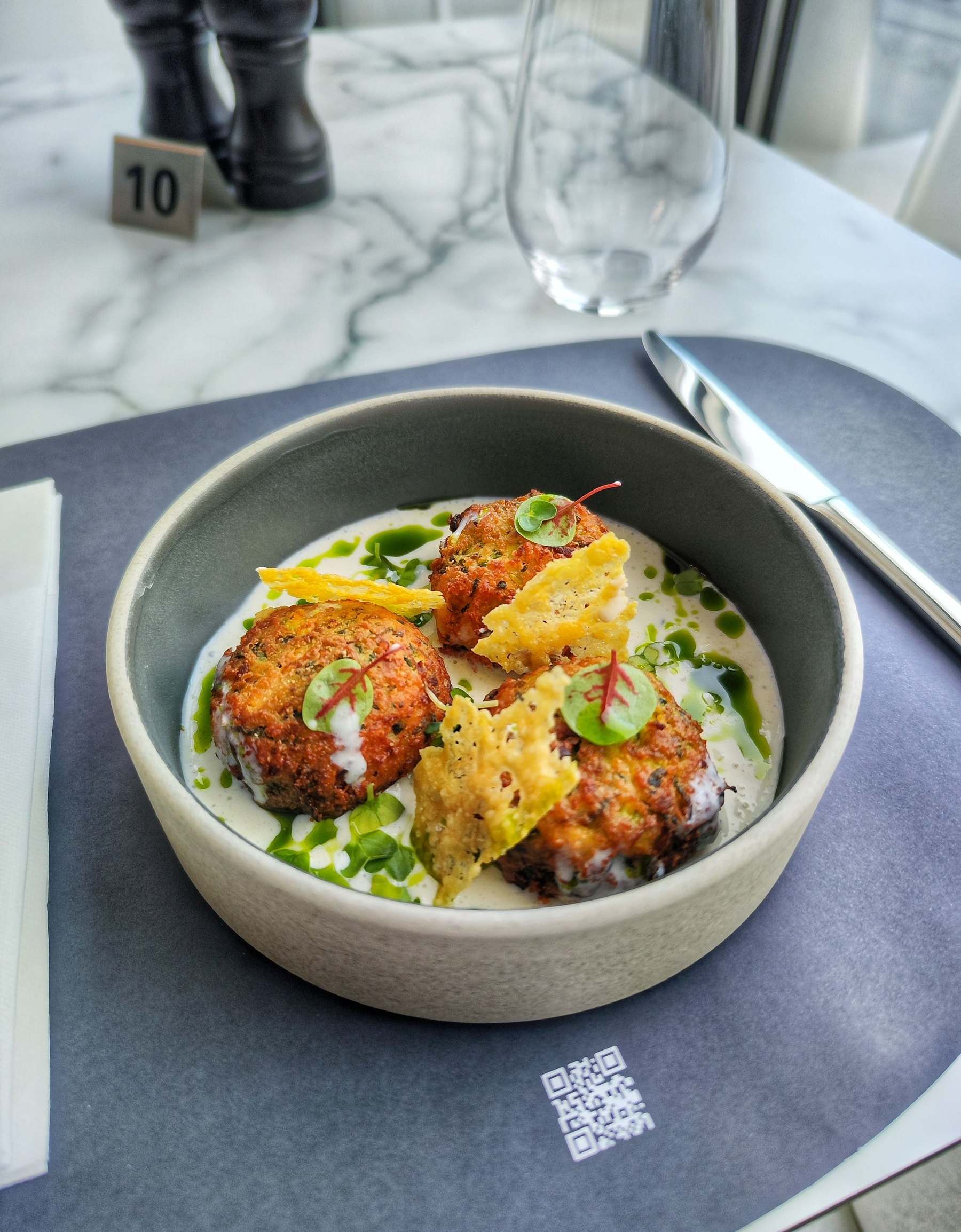 Golden zucchini fritters with parmesan crisps over yogurt in a grey bowl